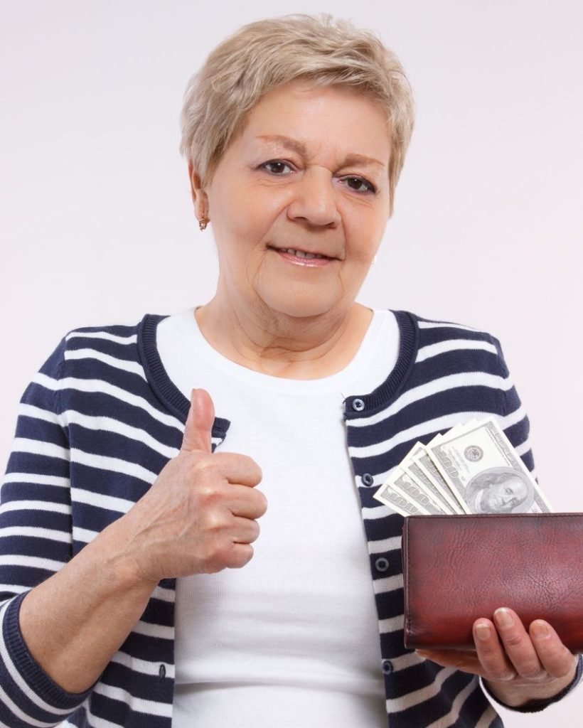 Senior woman holding wallet with dollar and showing thumbs up